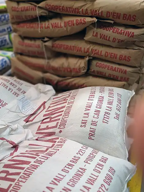 Sacs de subministraments agrícoles amb la marca de la Cooperativa Verntallat, apilats a la botiga de l’Agrari.