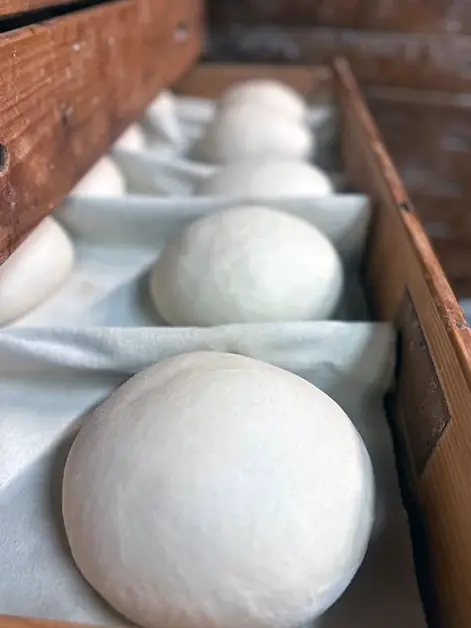 Boles de massa fermentant en calaixos de fusta, preparades per enfornar.