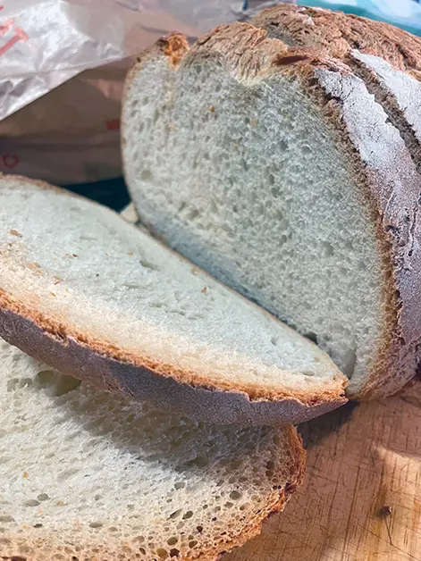 Pa blanc de crosta cruixent tallat a llesques sobre una fusta.